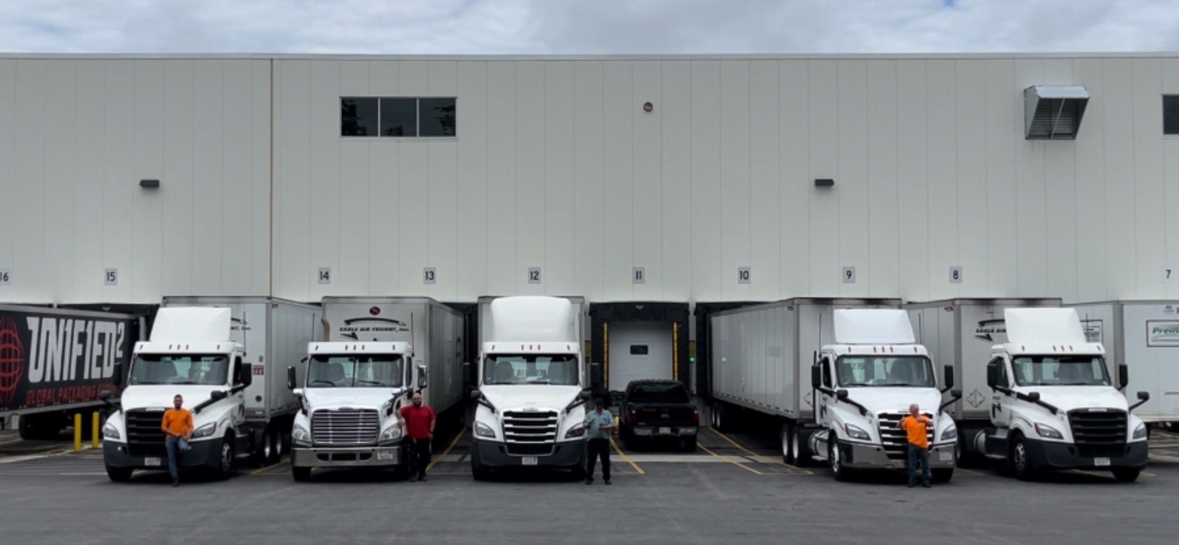 Several Eagle Air Freight semi-trucks lined up at numbered loading dock bays of a large warehouse facility.