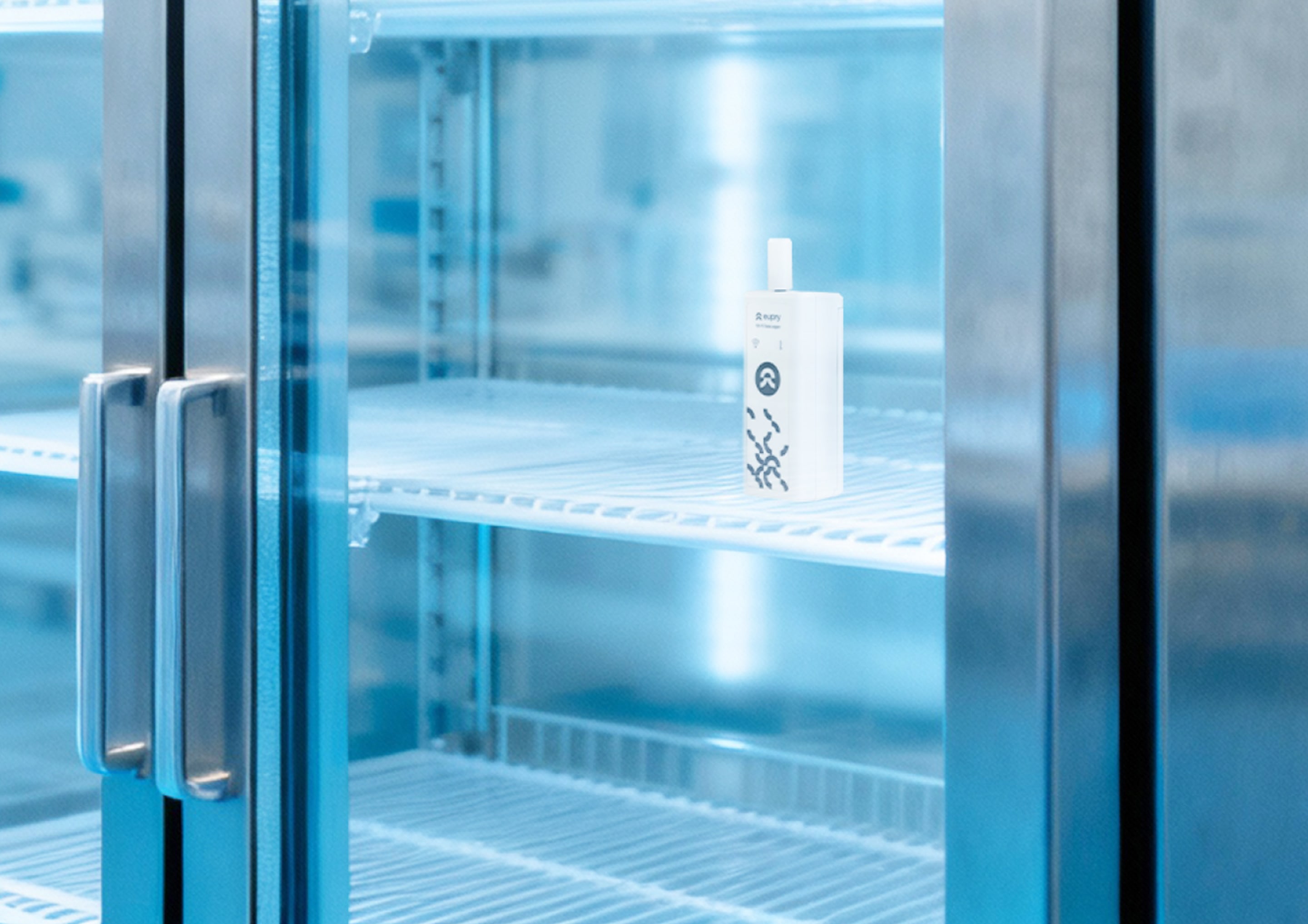 Eupry temperature data logger placed on a shelf inside an empty pharmaceutical refrigerator with glass doors