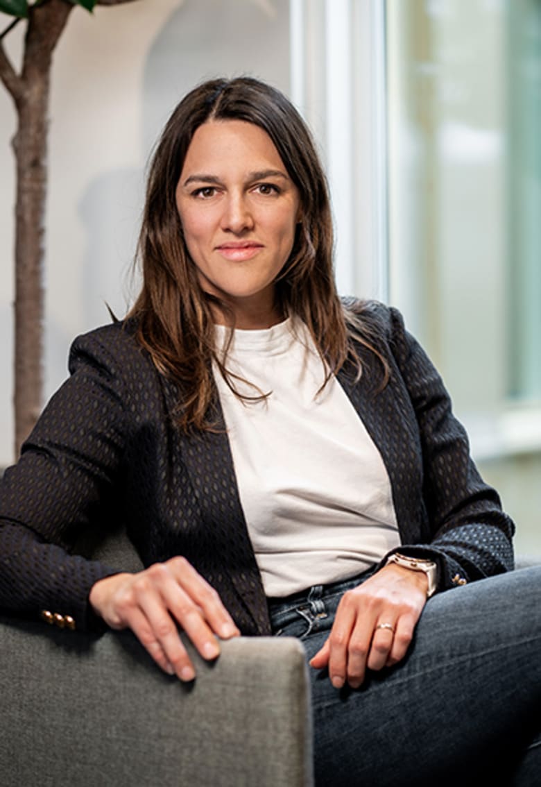 Woman in dark blazer and white shirt seated in modern office chair, looking directly at camera