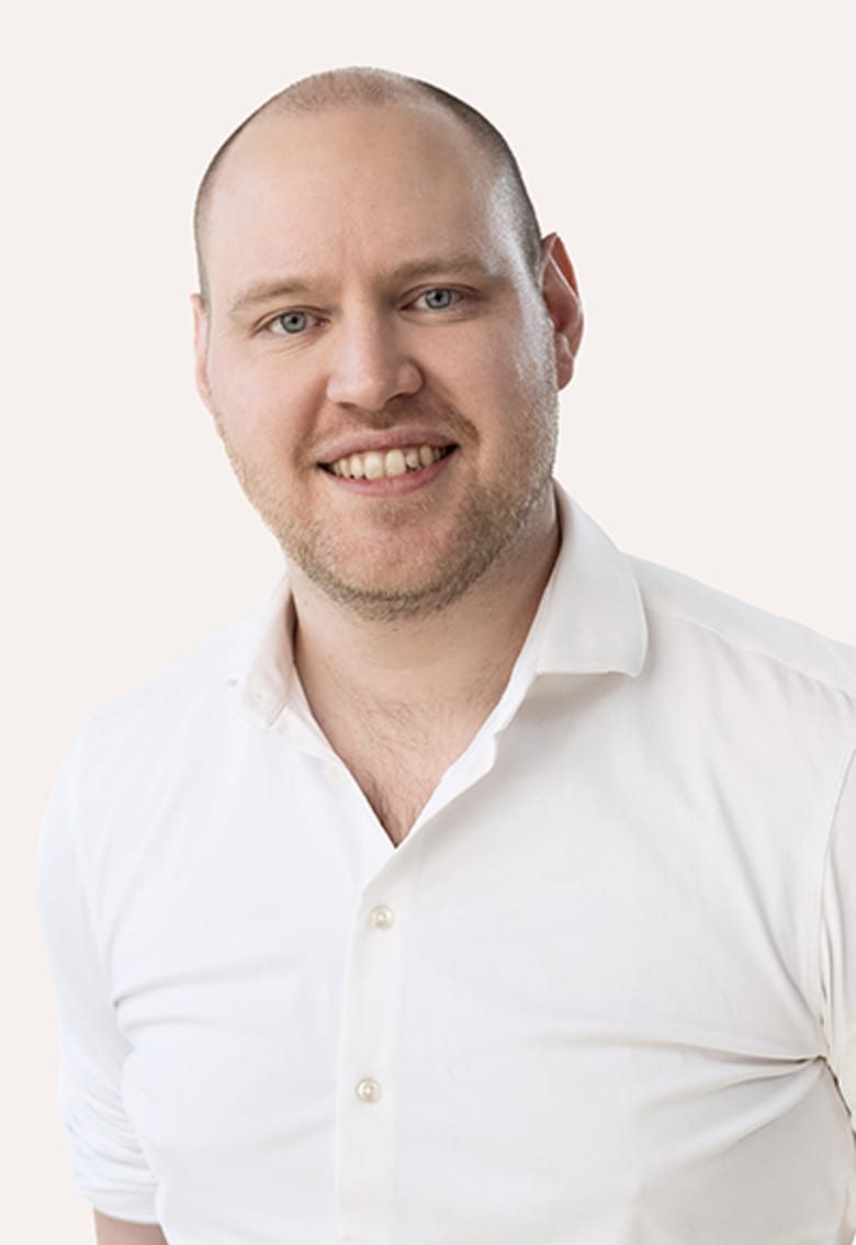 Smiling man with short hair wearing a white button-up shirt against a light background