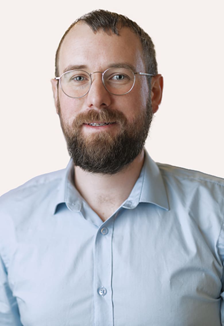 Headshot of Jakob, a bearded man with glasses wearing a light blue shirt, against a neutral background.