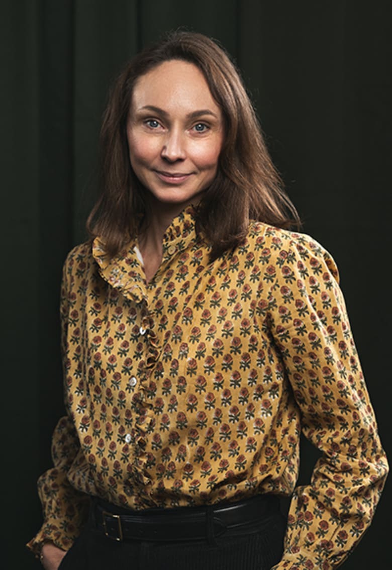 Woman in yellow floral blouse smiling, professional portrait against dark green background