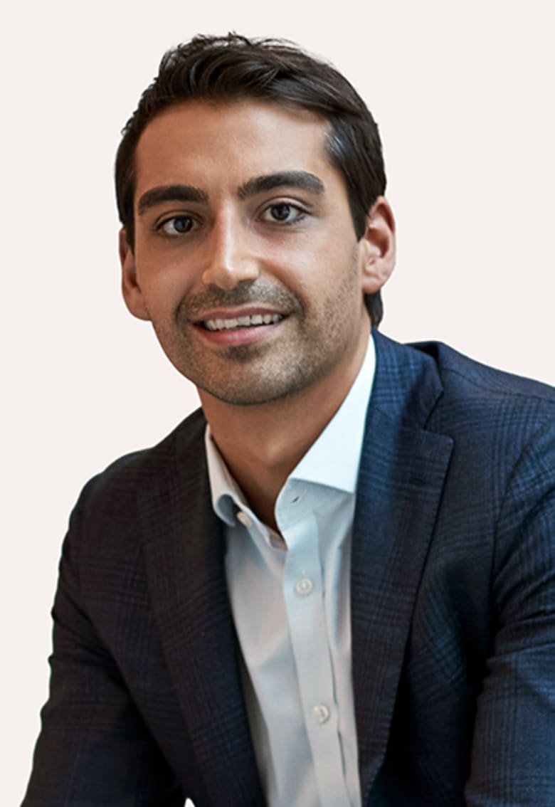 Smiling young professional man in a navy plaid blazer and light blue shirt against a light background