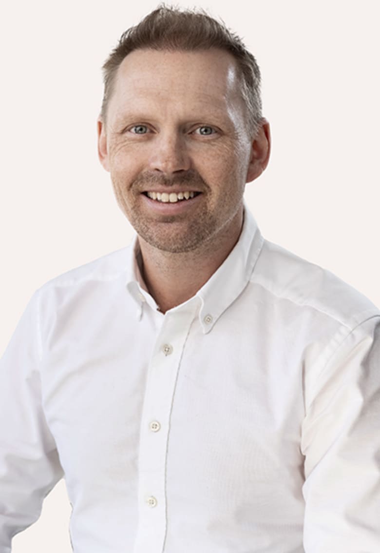 Smiling man with short hair and beard wearing a white button-down shirt against a light background