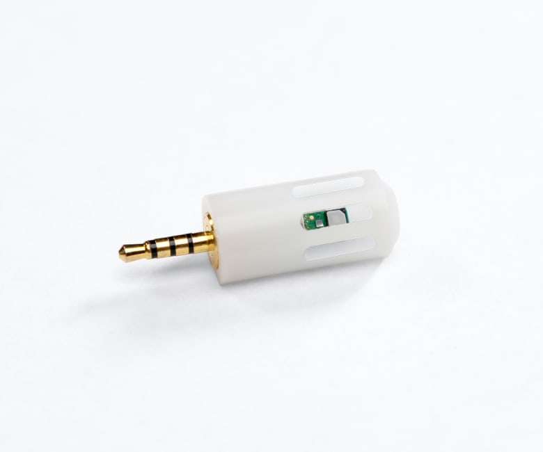 Small white cylindrical sensor with a 4-pole gold 3.5mm jack plug and visible green PCB through ventilation slots.