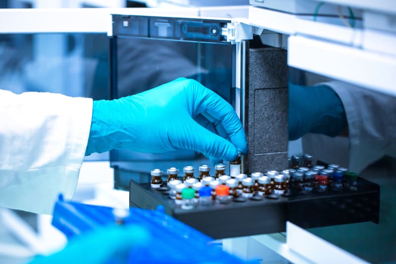 Gloved hands loading sample vials into an autosampler tray on a laboratory analytical instrument