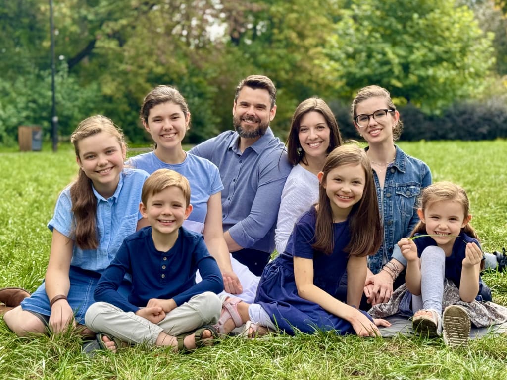 The Steele family, Joshua and Kelsie with their six children, sitting together on the grass in a park