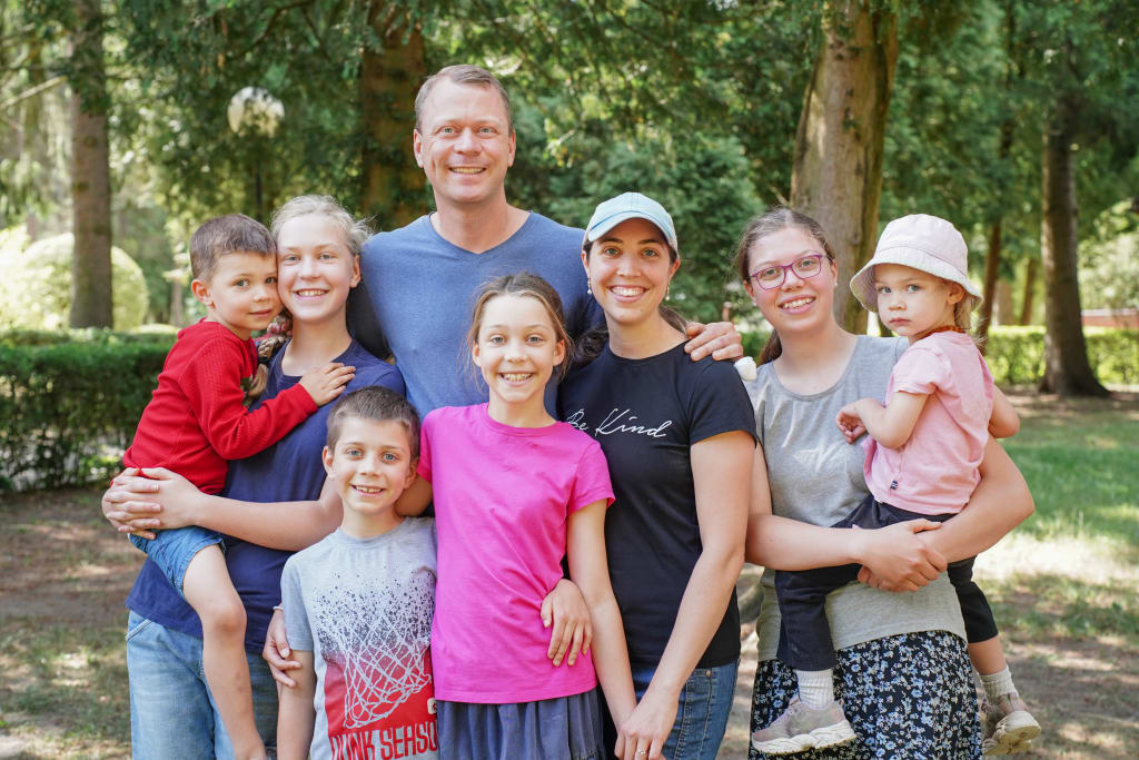 The Day family, Nathan and Katelin with their six children, standing together under the trees