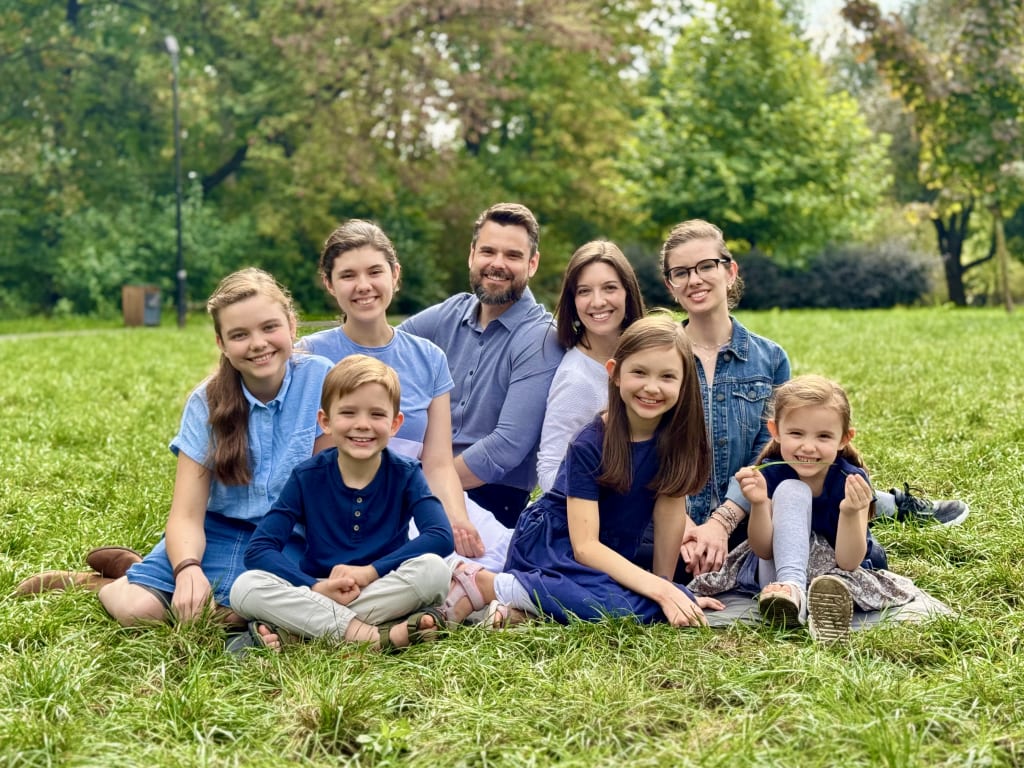 The Steele family, Joshua and Kelsie with their six children, sitting together on the grass in a park