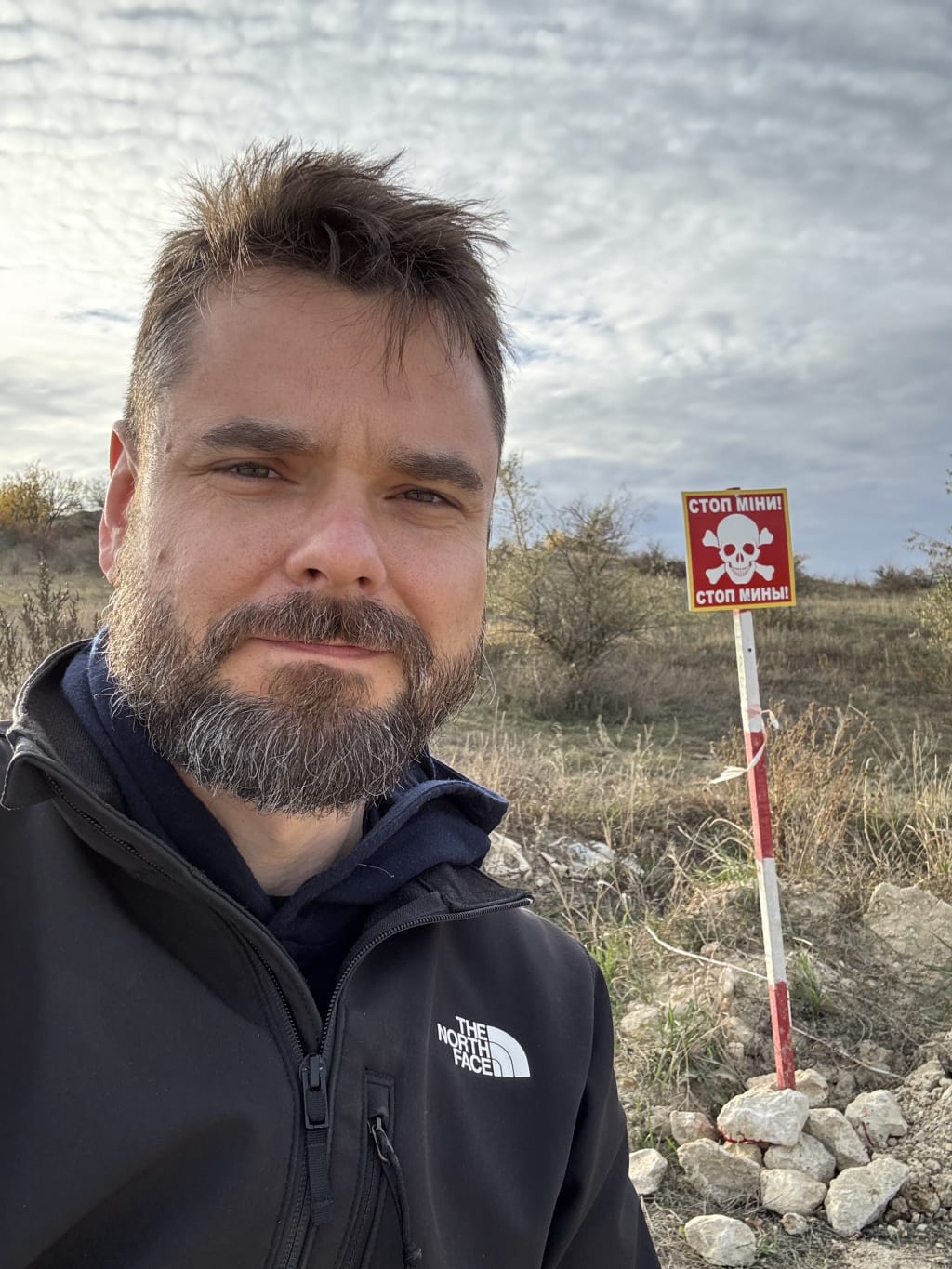 A hand-painted red sign at the edge of a field reads "Stop — Mines" in Ukrainian and russian.