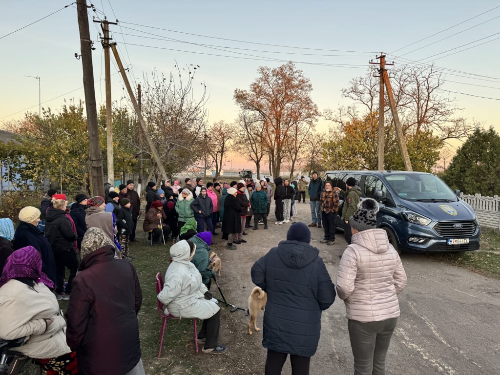 Villagers gather around the team's van at dusk while a team member preaches.