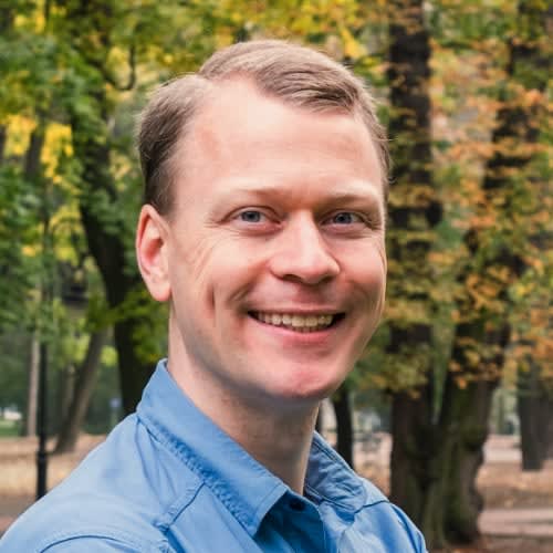 Smiling, in a park with autumn trees behind him.