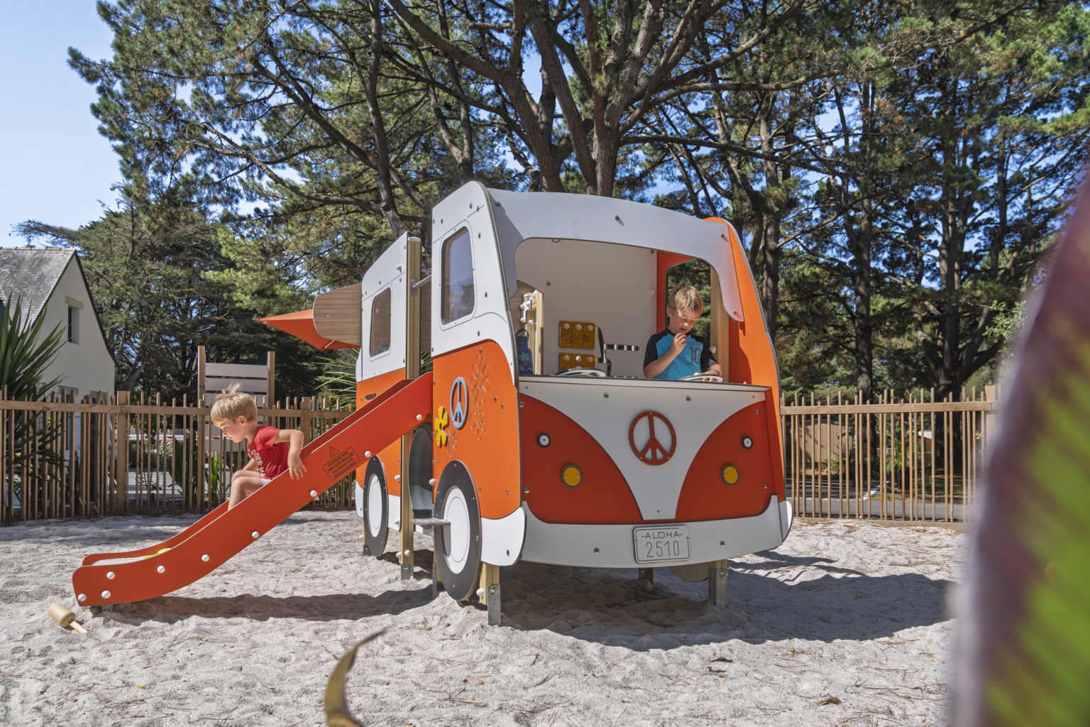 Child going down the small slide attached to campervan feature in play area at Camping Parc Sainte-Brigitte in Brittany