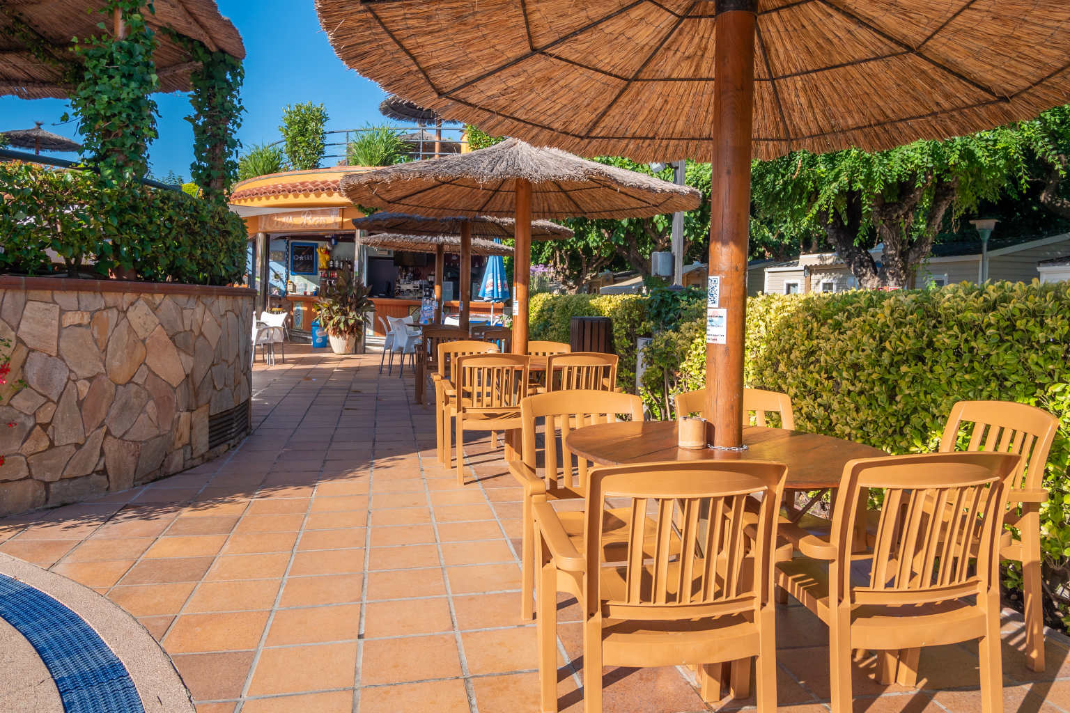 Bar terrace tables under parasols, next to the central pool at la Masia campsite, Blanes, Costa Brava
