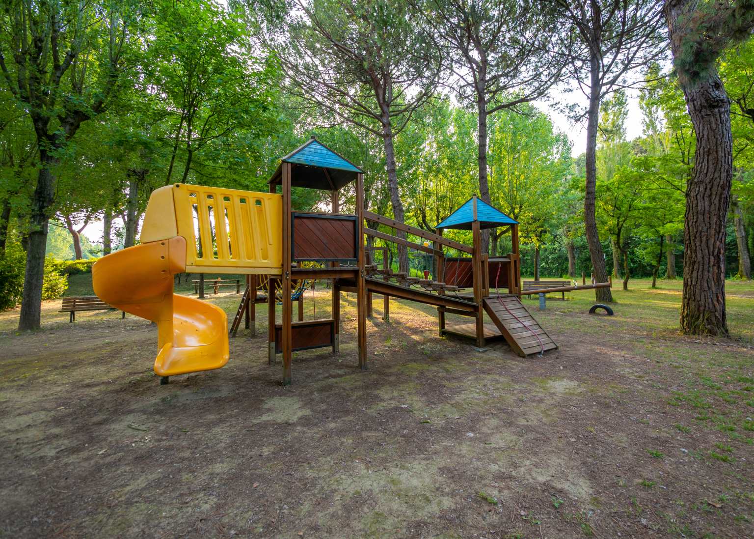 Play area under trees with wood/plastic equipment - bridge to small slide, climbing net, at Portofelice camping village, near Venice