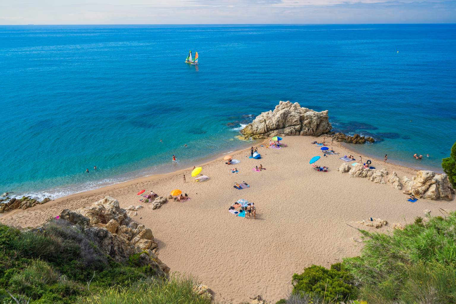 People sunbathing on triangle of beach, sailing boats in the sea, close to Roca Grossa campsite, Callela, Costa Brava