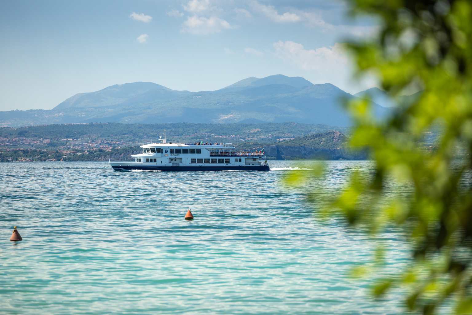 Pleasure lake cruise boat sailing past Cisano San Vito campsite on Lake Garda