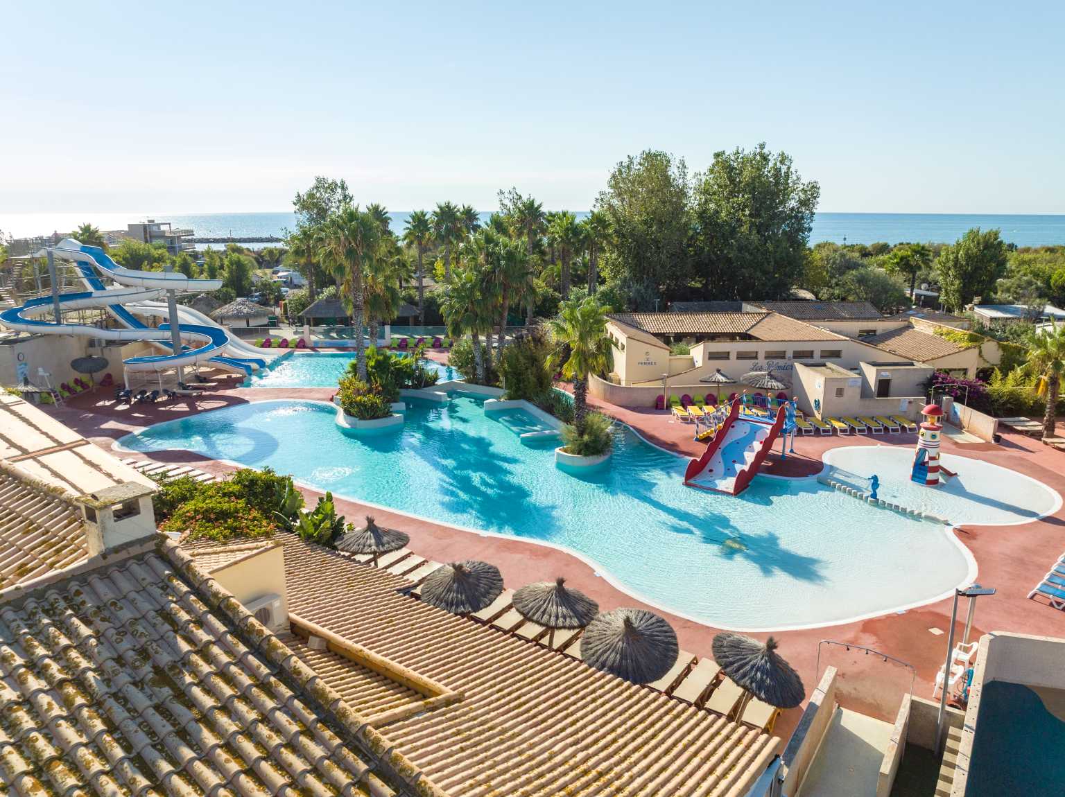 Aerial view of lagoon pool with lighthouse feature, kids slide and waterchute at Plage et le Bord de Mer campsite, Languedoc