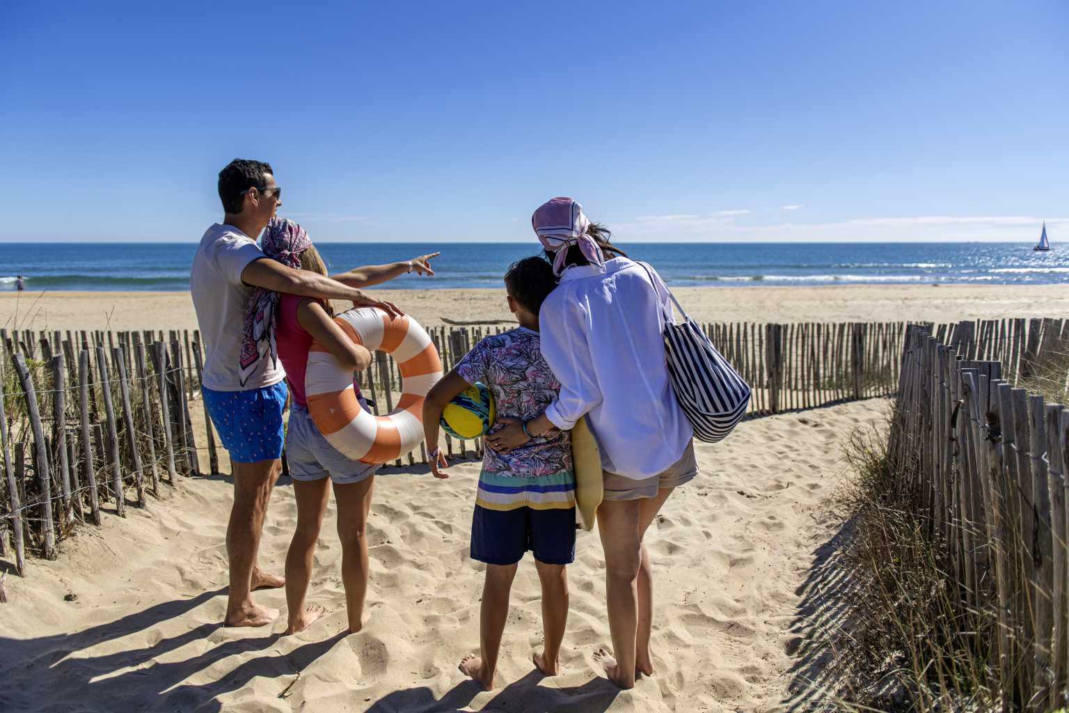 Family walking down the beach path with inflatable swimming ring, at Le Castellas campsite in the Languedoc