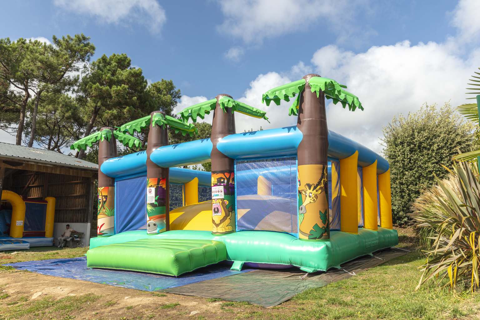 Large bouncy castle with 4 inflatable palm tree features on the front wall, in front of the play barn at le Mane Guernehue campsite Brittany