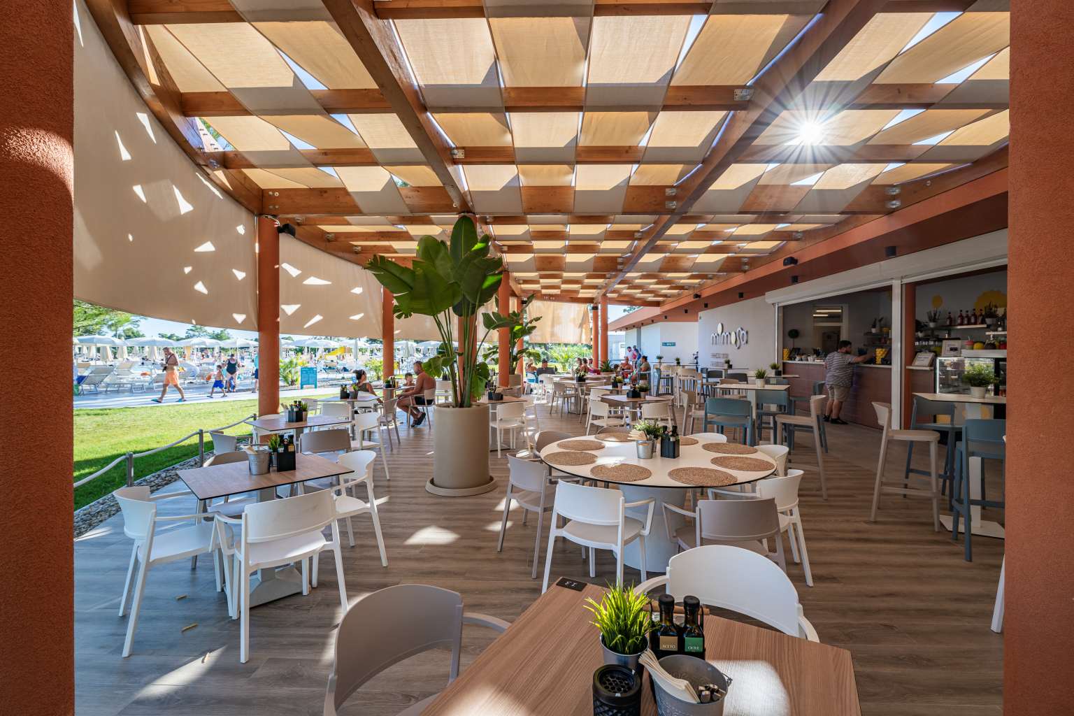 People sitting at shaded tables under an awning at the Mimosa bar restaurant at Zaton Holiday Resort, in Dalmatia, Croatia