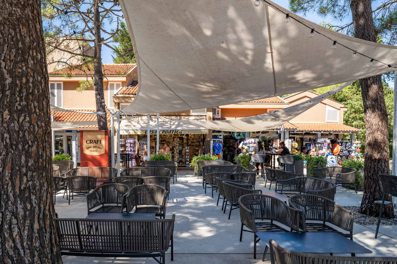 Chairs under sail canopy, looking across to gift shop and craft beer garden sign at Zaton Holiday Resort, in Dalmatia, Croatia