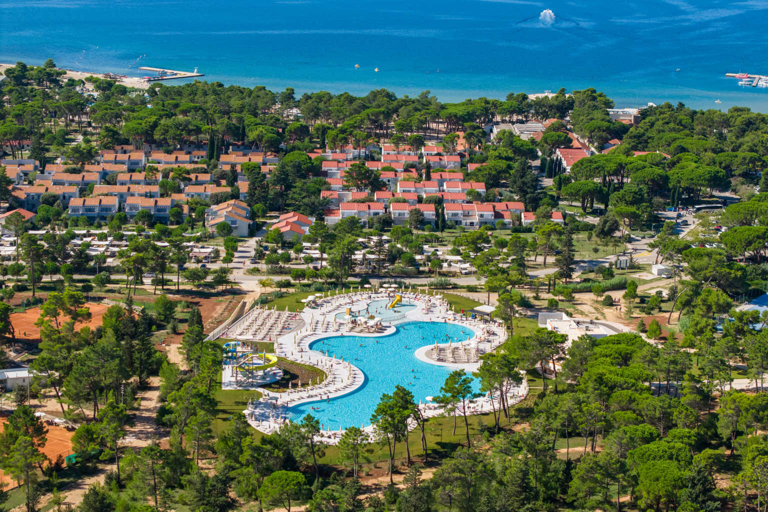 Aerial view of the lagoon pool complex surrounded by trees, nearby apartments and view of the sea, at Zaton Holiday Resort, in Dalmatia, Croatia