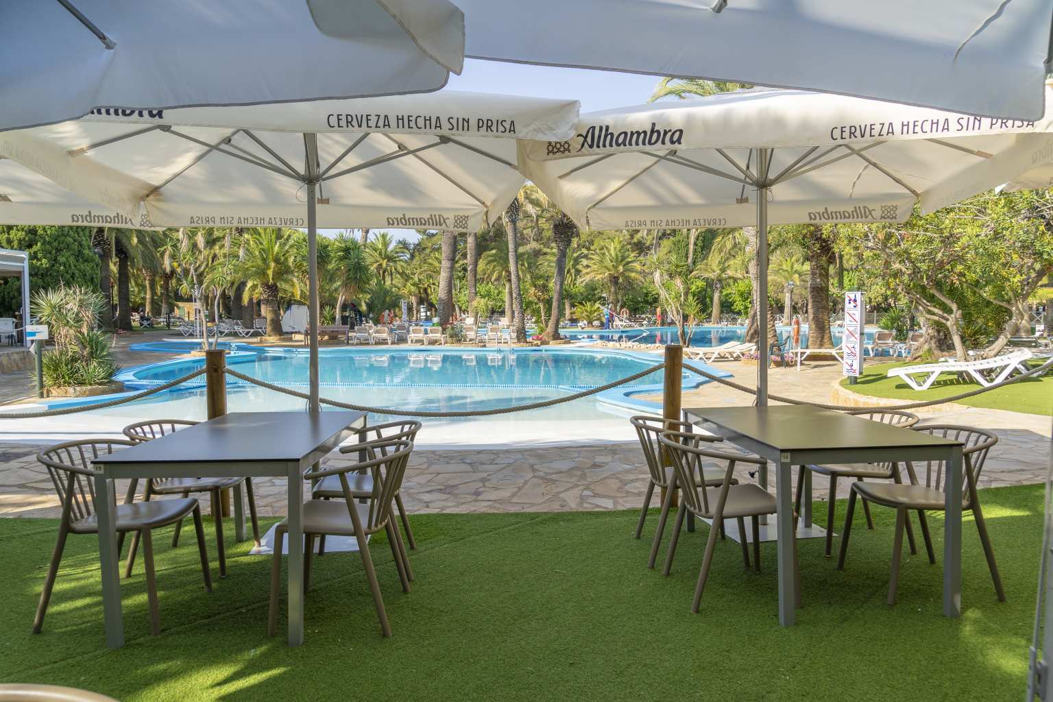 Pool bar terrace tables and parasols on the lawn overlooking the pool at La Torre del Sol campsite, Miami Platja, Costa Dorada