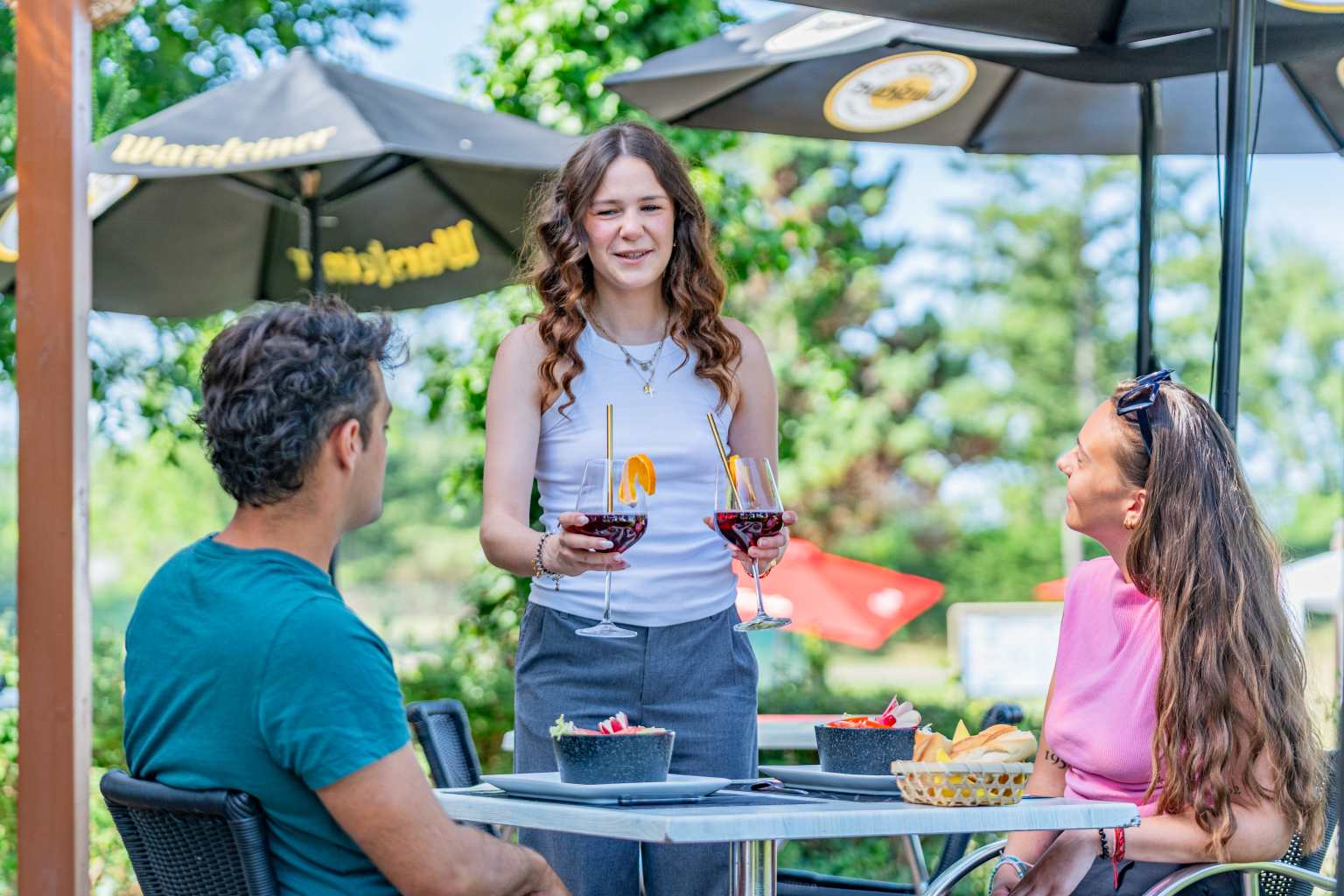 Waitress serving drinks to customers on the bar terrace at L'Ile du Rhin campsite, Alsace, France