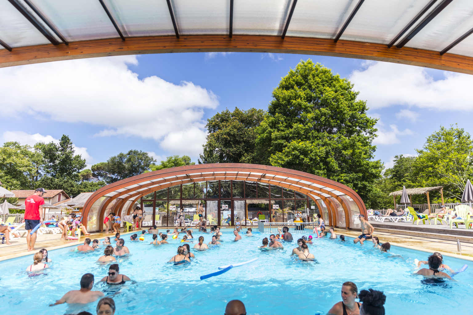 Lots of people swimming in the covered pool, canopy open, at Le Soleil des Landes campsite in Landes, France