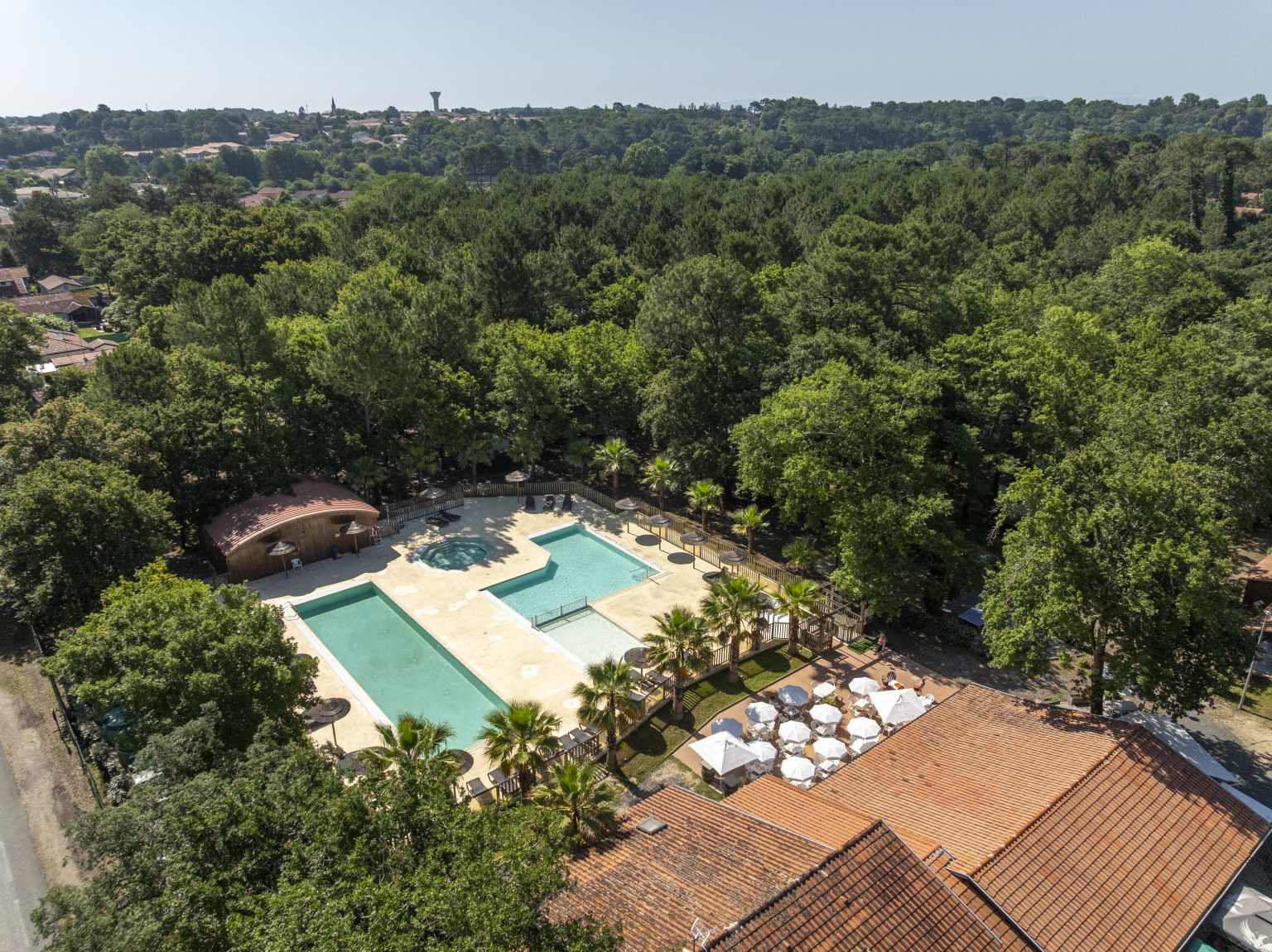 Aerial view of the jacuzzi pool, rectangular pool and kids pool and wooded countryside at Lou Pignada campsite, Ondres Landes
