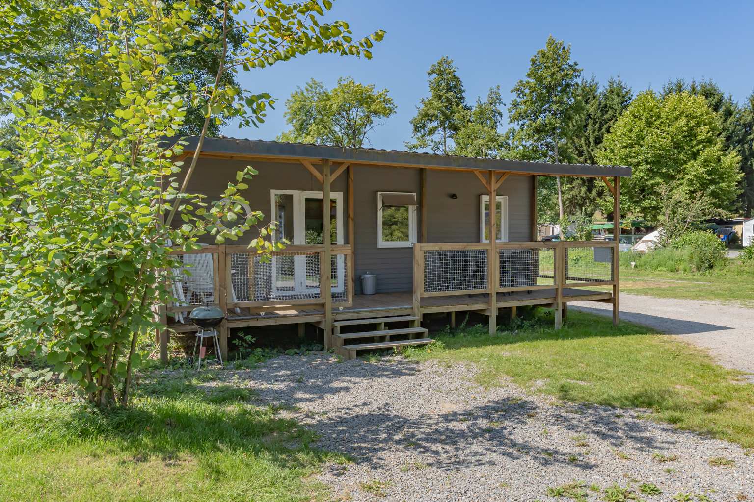 Holiday home accommodation on a grassy pitch with scattered trees and fully covered decking at Kinzigtal campsite in the Black Forest in Germany