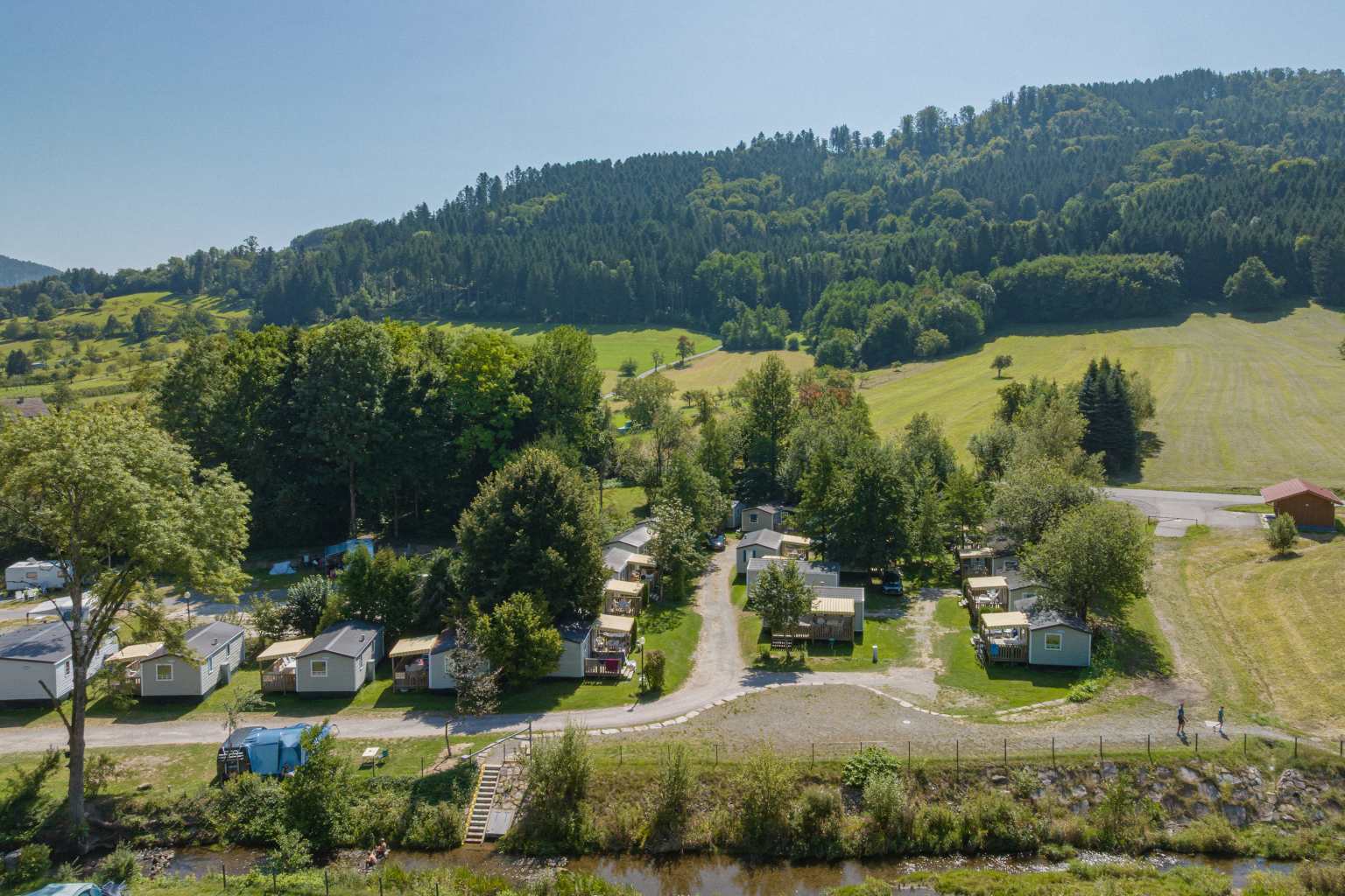 Aerial view of the holiday homes under the trees on the edge of the Kinzigtal campsite in the Black Forest in Germany, with the hills and fields rising beyond at the edge of the site
