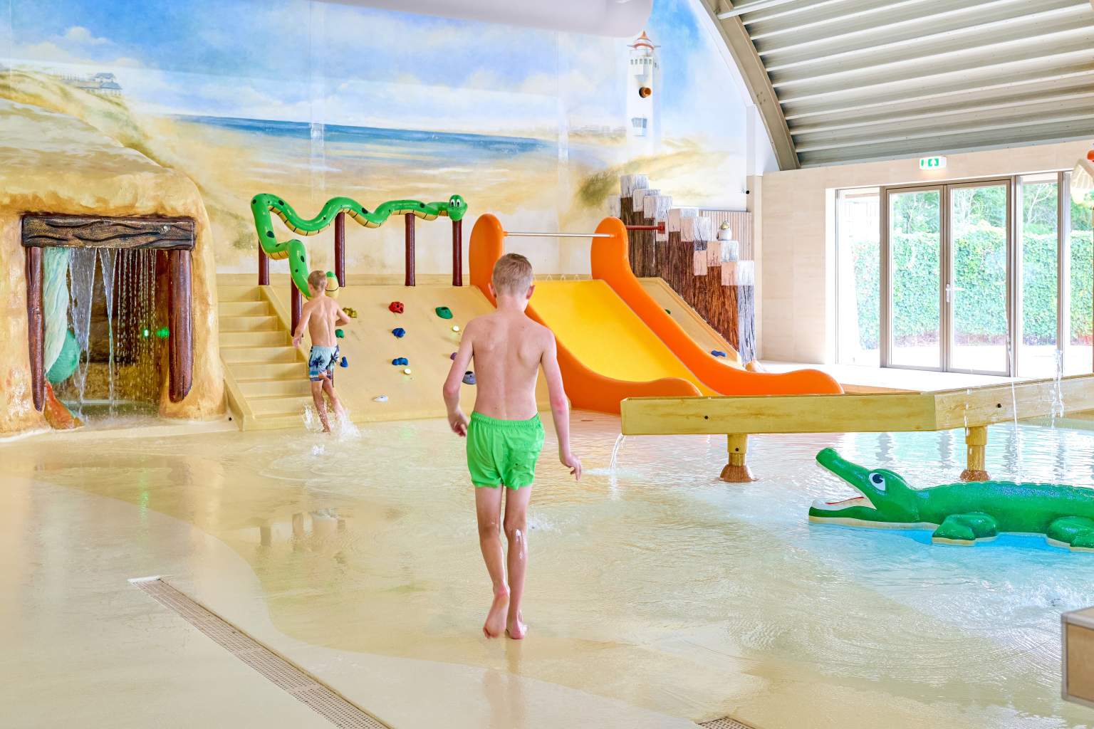 Boy walking in the indoor pool besides the shallow area for toddlers with crocodile feature, near the waterslide, Koningshof campsite, in South Holland