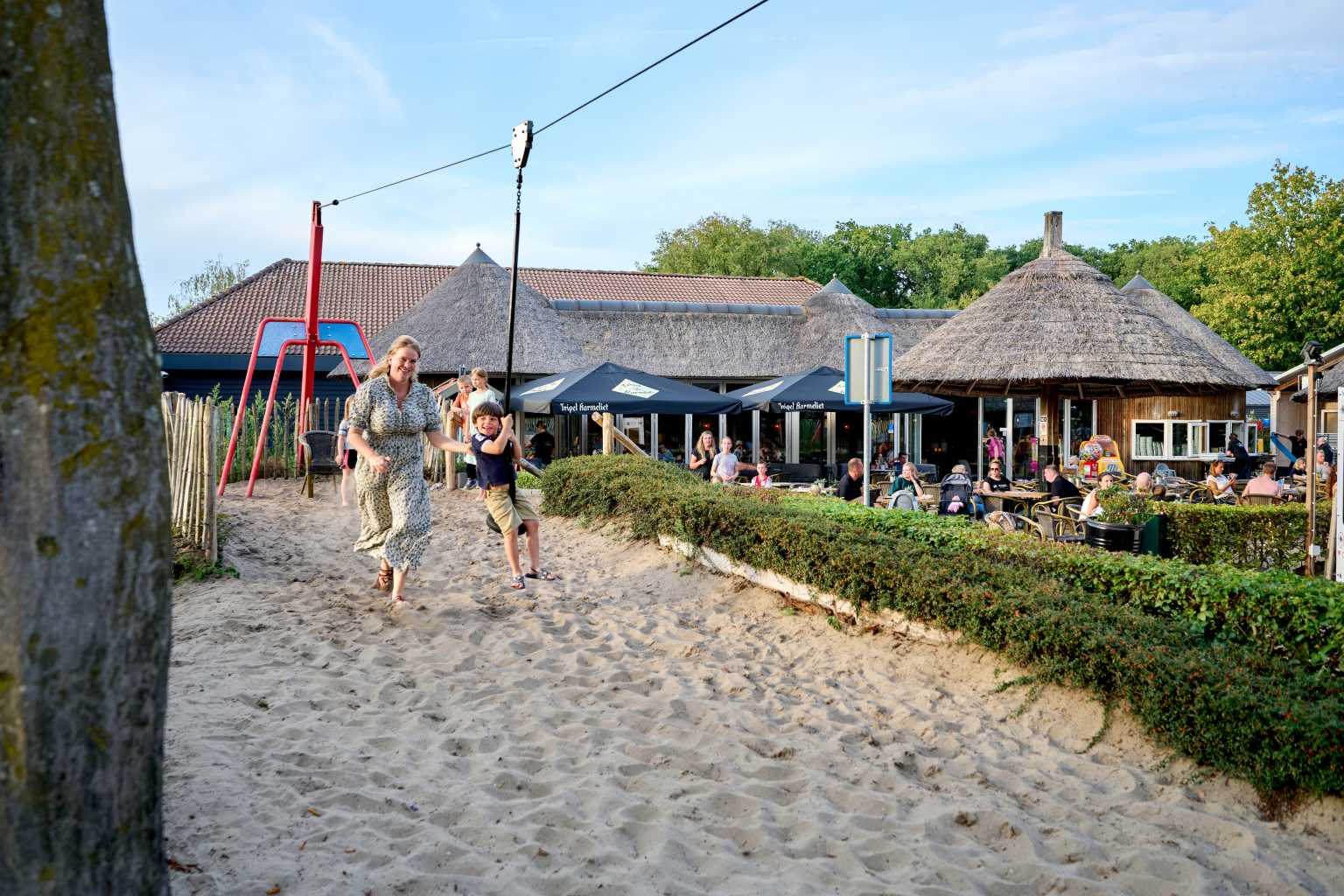 Child on the button zip wire with mother in the play area next to the thatched restaurant at Marvilla Parks Kaastsheuvel, North Brabant, Netherlands