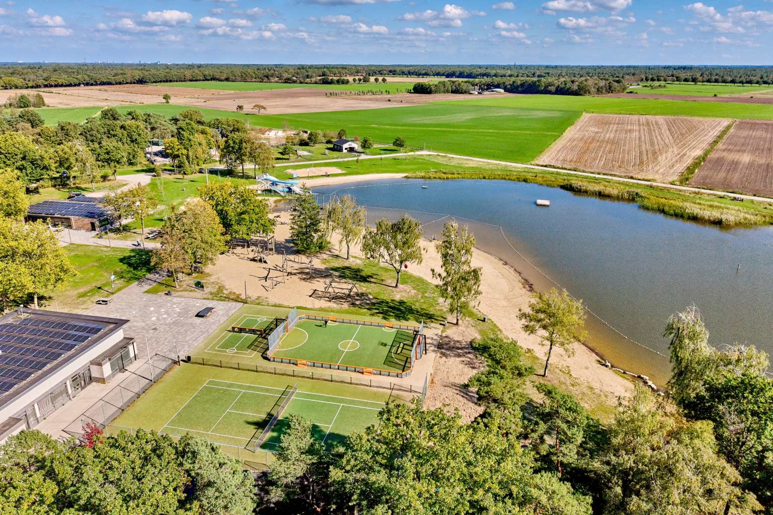 Aerial view of the lake, beach, tennis court and football pitch at De Flaasbloem campsite in the Netherlands