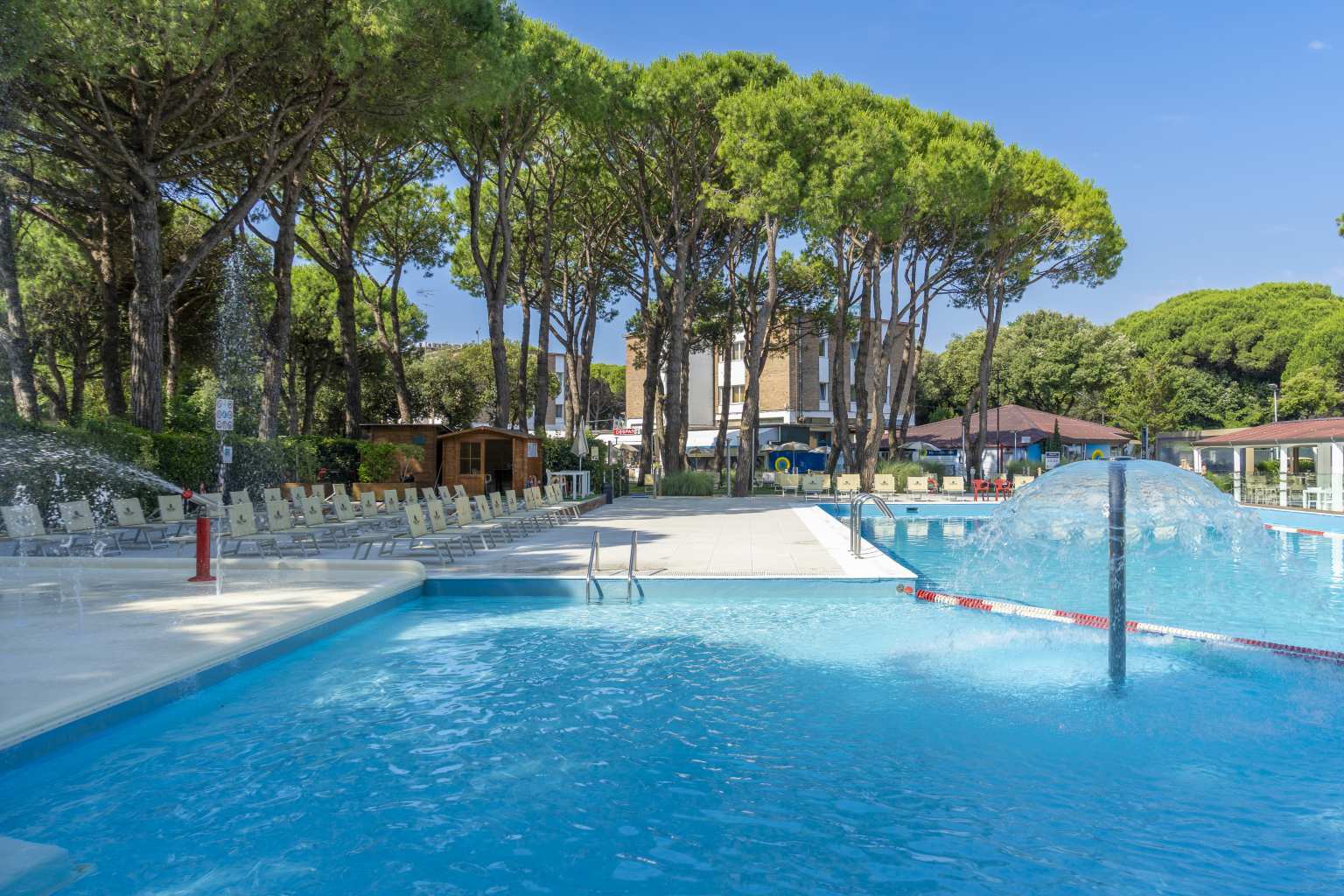 Water mushroom feature in paddling pool, next to rectangular pool, shaded by trees at at Jesolo Mare Camping Village, Adriatic, Italy