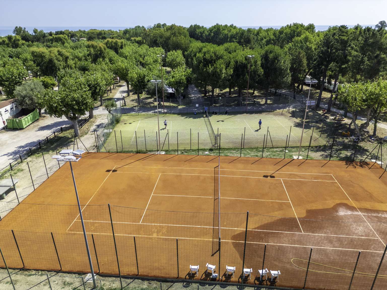 Aerial view of hard surface - orange - tennis court and behind, multi sports court with game of tennis, at Roseto degli Abruzzi campsite, Abruzzo, Italy 