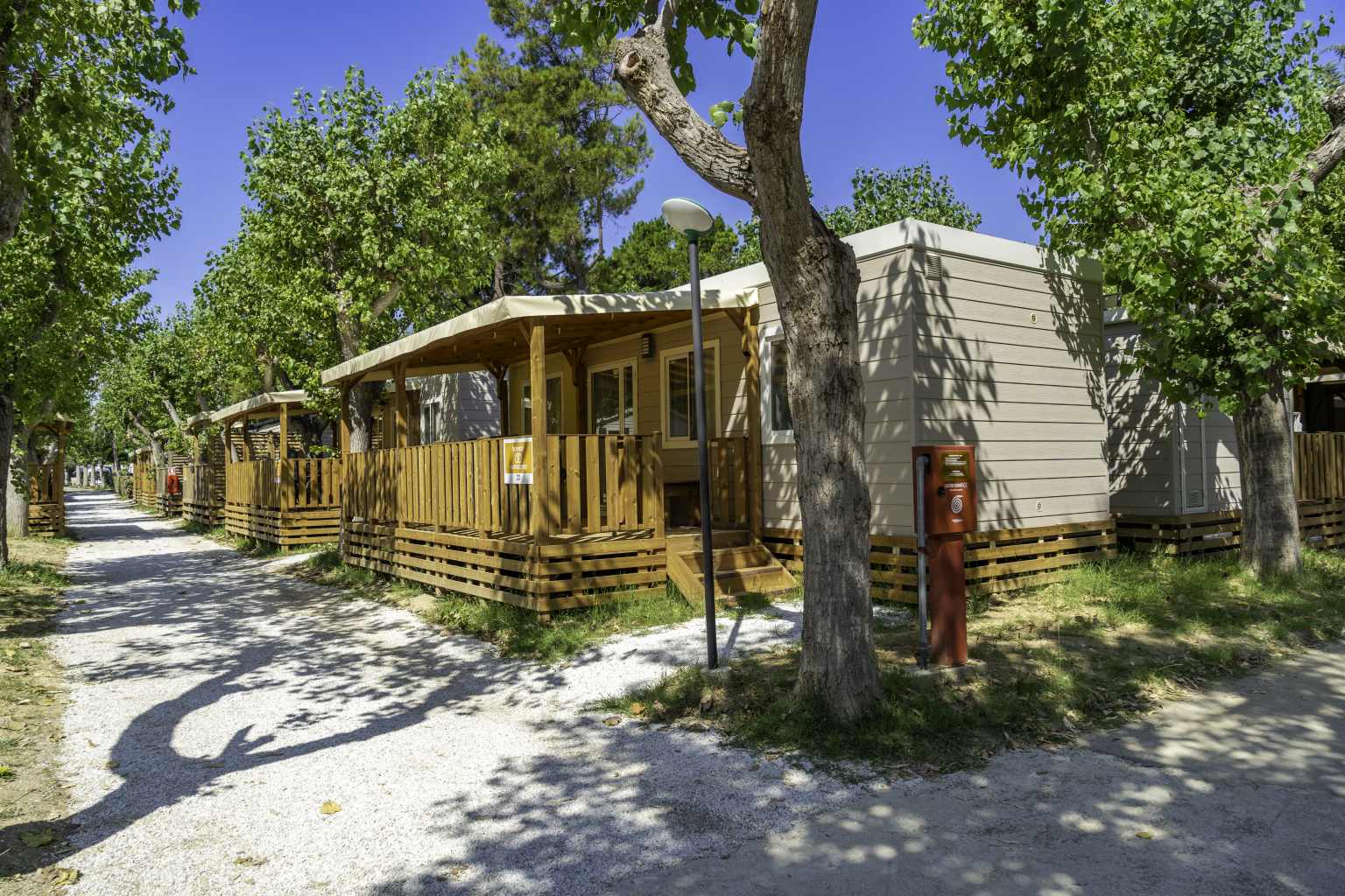 Lane of two rows of holiday home accommodation, all with covered decking, at Roseto degli Abruzzi campsite, Abruzzo, Italy