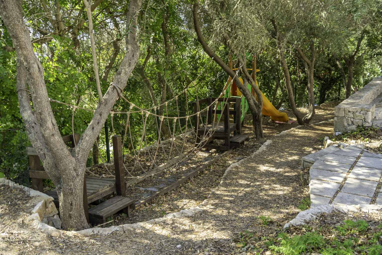 Play area with rope bridge under the trees at La Scogliera campsite, Puglia