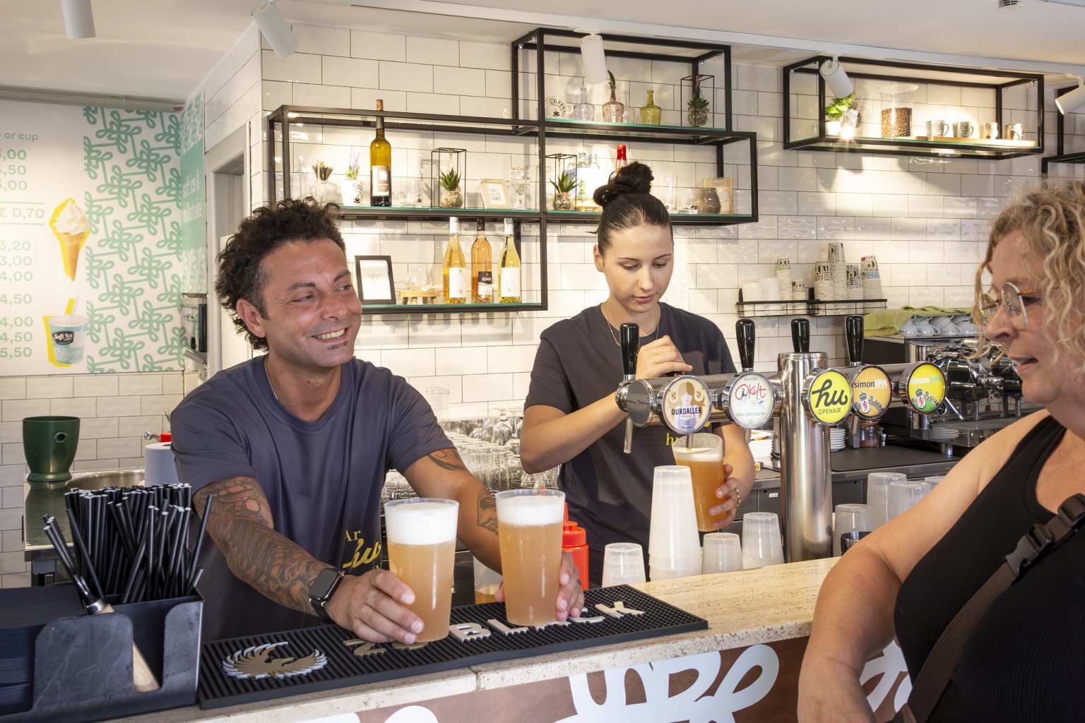 2 staff serving drinks to a customer at the bar at Hu Birkelt Village campsite in Luxembourg