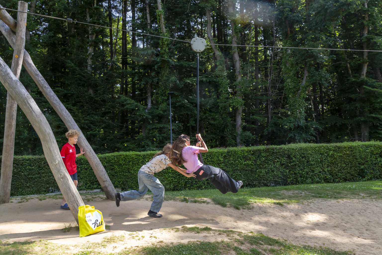 3 older children playing on the button zip wire on the play area at Hu Birkelt Village campsite in Luxembourg