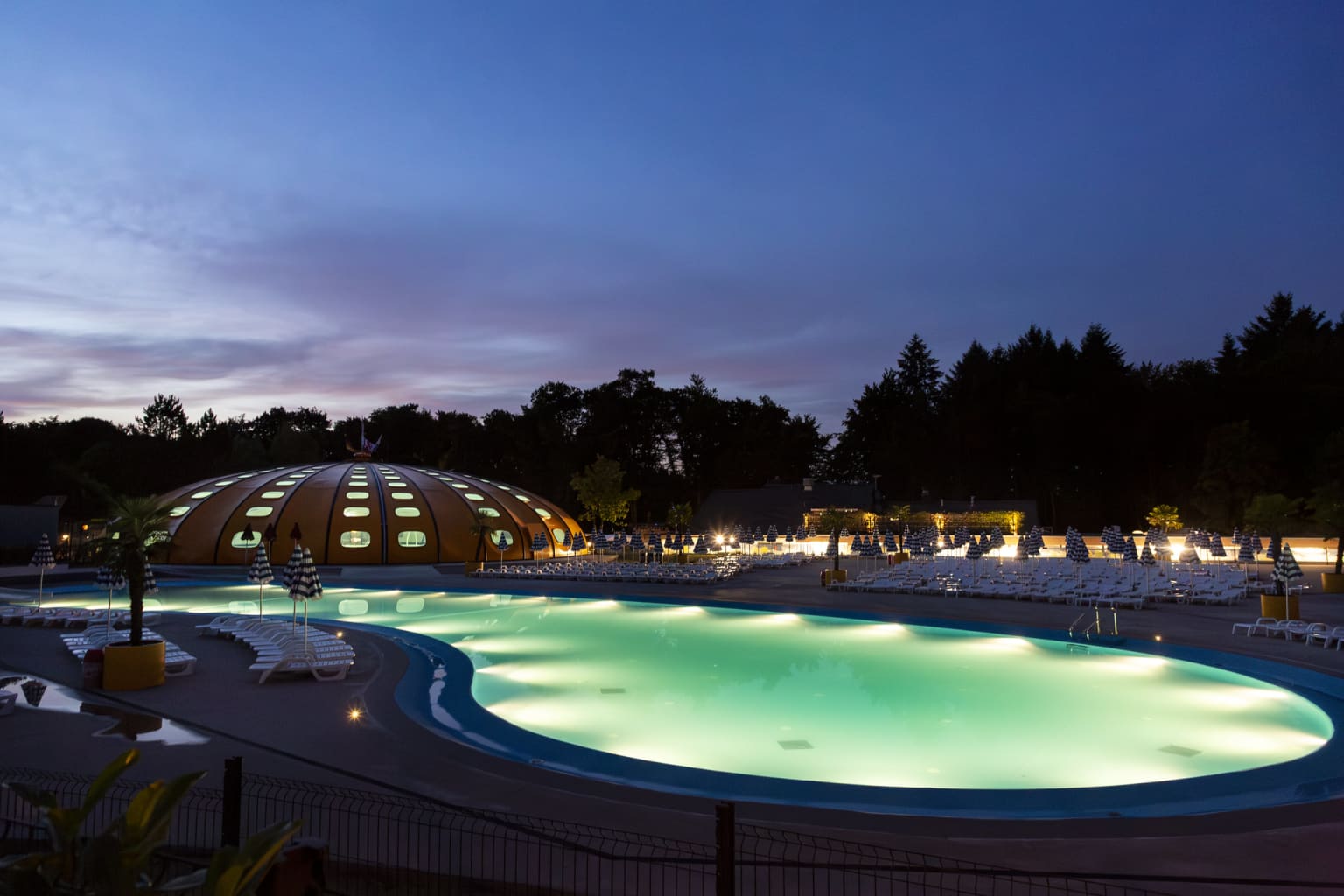 Outdoor pool and dome pool lit up at night at Hu Birkelt Village campsite in Luxembourg