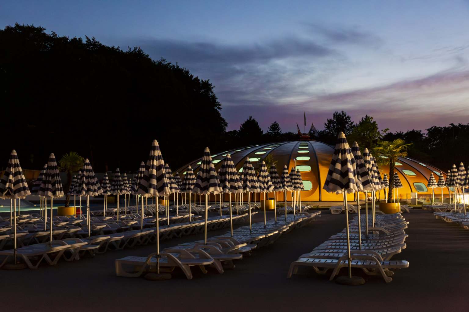 Sunlougners and the dome pool lit up at night time at Hu Birkelt Village campsite in Luxembourg