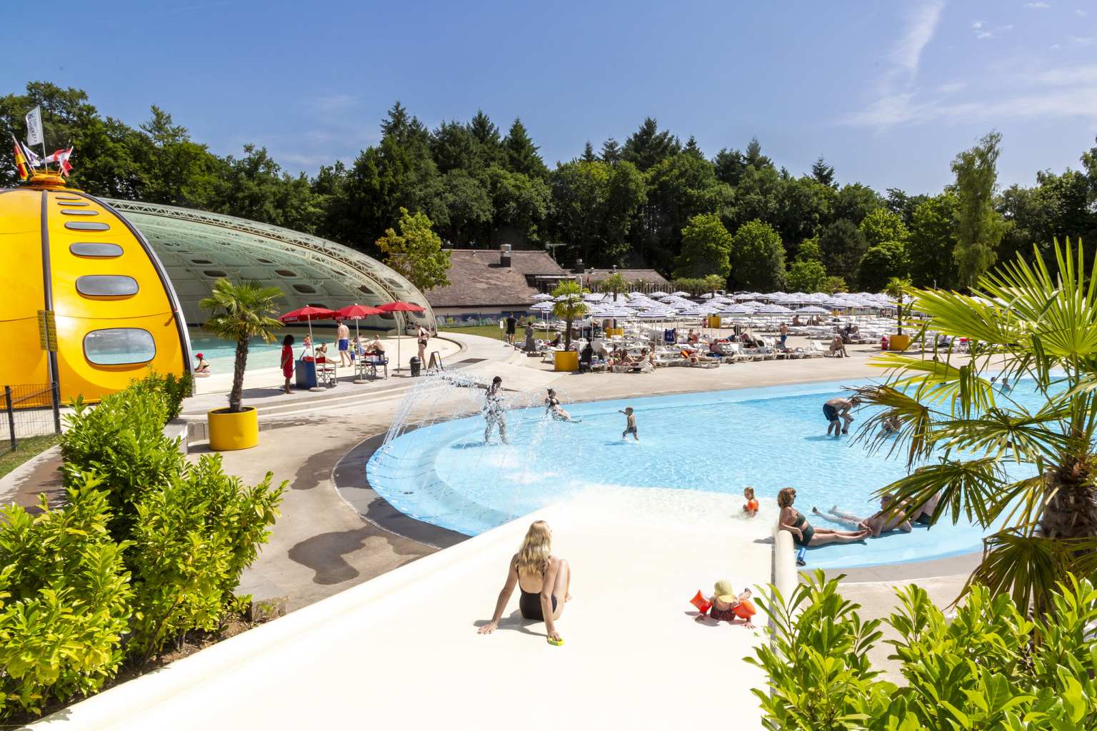 Lady sliding down the water slope into the lagoon pool, dome indoor pool to the left, at Hu Birkelt Village campsite in Luxembourg