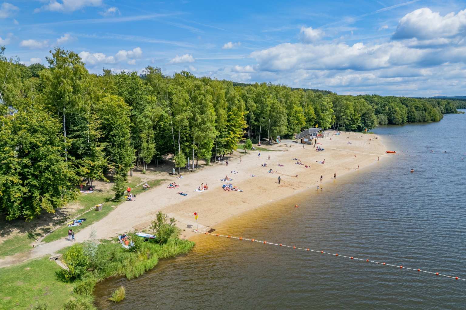 Aerial view of the sandy lake beach, backed by trees, at Lac des Vielles Forges campsite in the Ardennes
