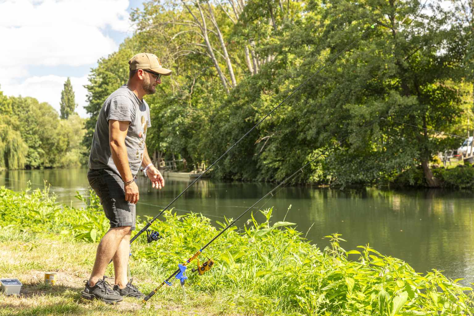 Fisherman checking two fishing rods on the banks of the river next to Les Fontaines campsite, Ivry-la-Bataille, France