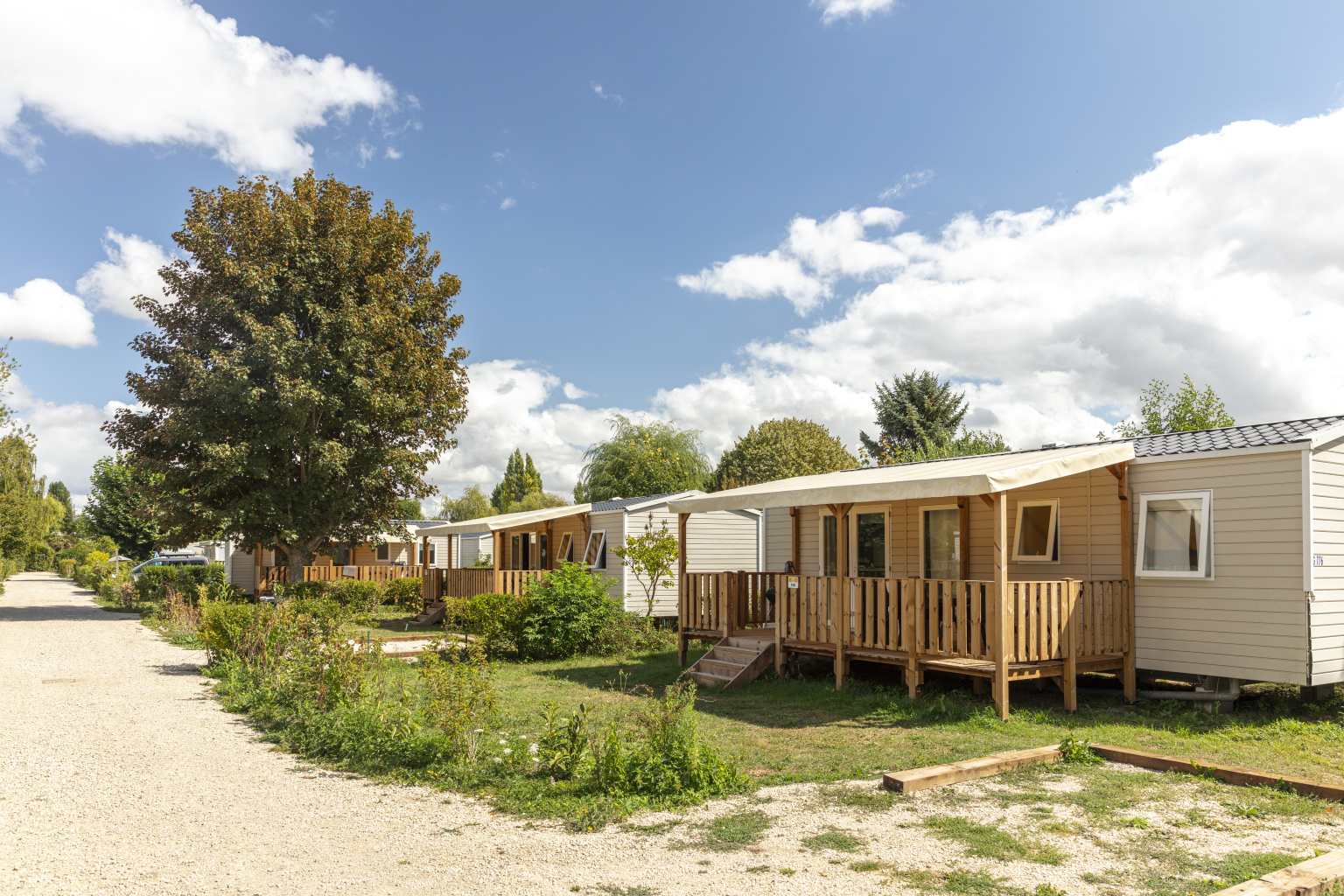 Row of sunny holiday homes with covered decks beside the park road at Les Fontaines campsite, Ivry-la-Bataille, France