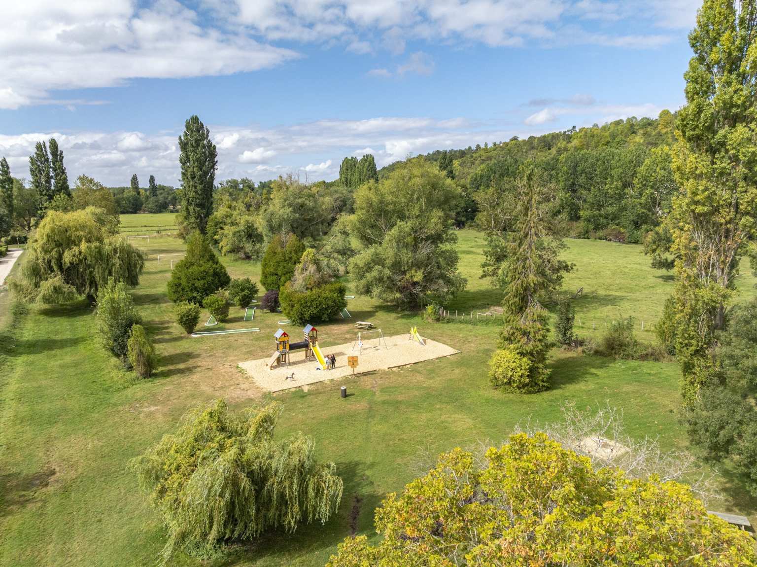 Aerial view of the play area surrounded by large grassy area and scattered trees at Les Fontaines campsite, Ivry-la-Bataille, France