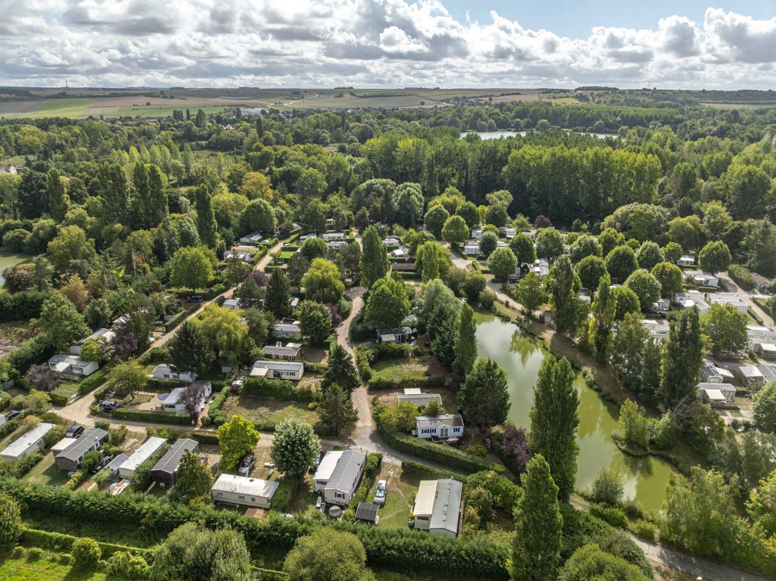 Aerial view of the holiday home, woods and small lake on site at Les Fontaines campsite, Ivry-la-Bataille, France